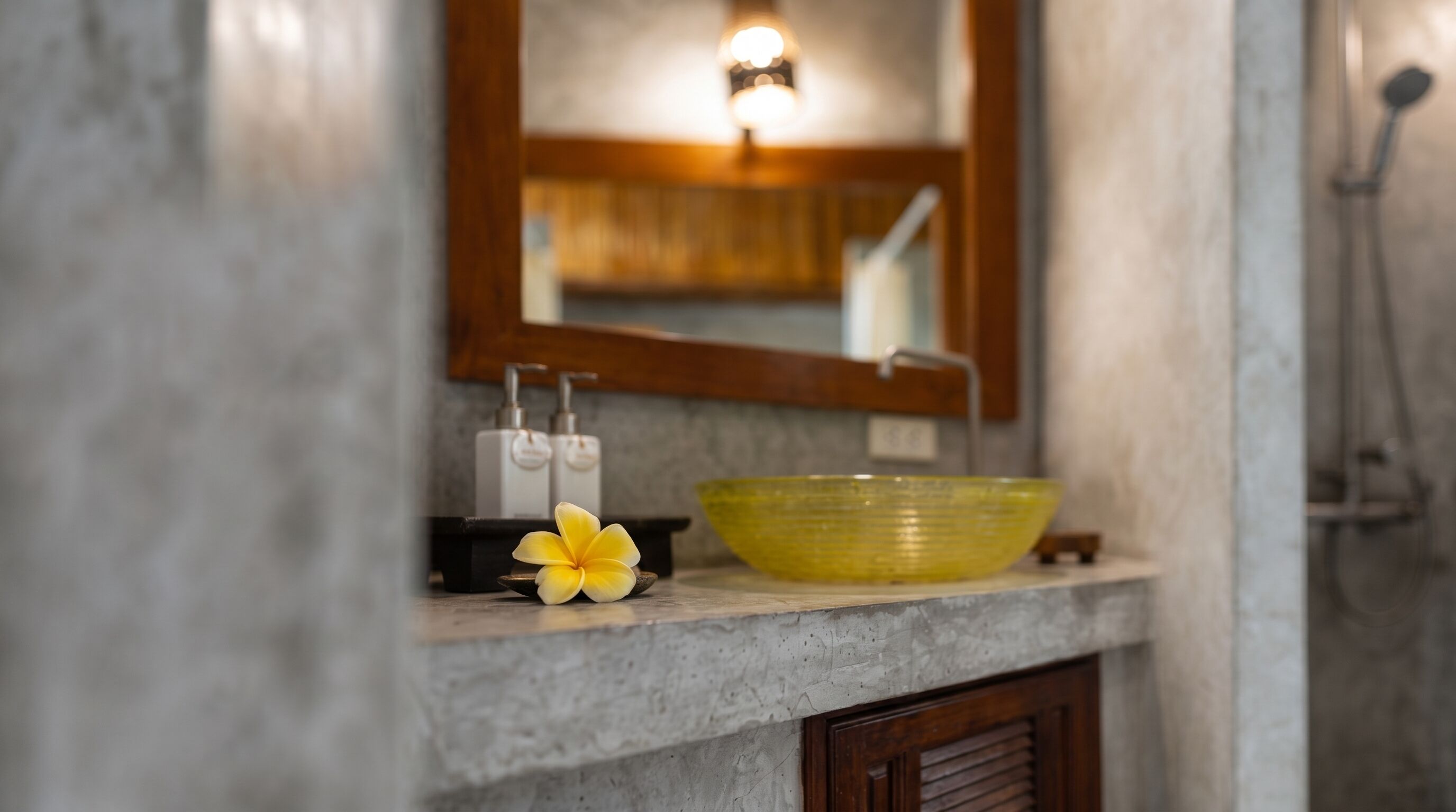Un baño con lavamanos de mármol, un cuenco amarillo y un armario de madera.