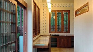 Un pasillo estrecho con puertas y ventanas de madera, un lavamanos pequeño y una lámpara.