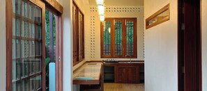 Un pasillo estrecho con puertas y ventanas de madera, un lavamanos pequeño y una lámpara.