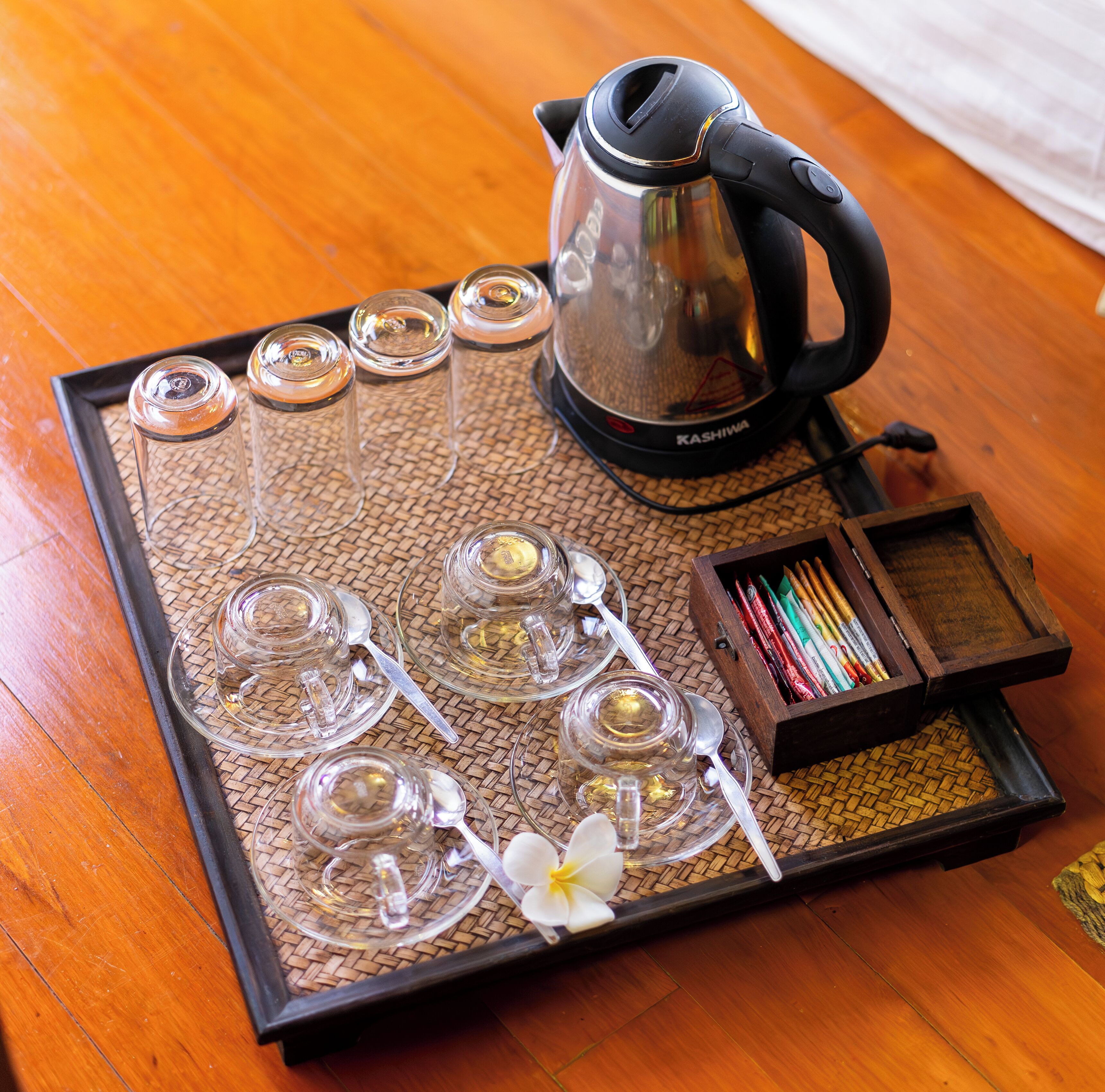 A tea set with a kettle, cups, and a box of pencils on a woven mat.