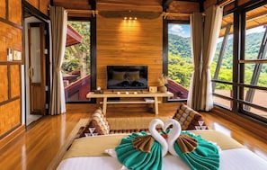 A room with a bed, a TV, a wooden desk, and large windows with a view of greenery. - Alama Sea Village Resort (Ko Lanta)