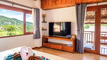 A hotel room with a large TV, wooden furniture, a bed with a decorative swan, and a balcony with a view of the hills.