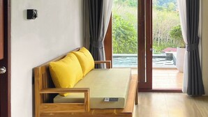 Una habitación con sofá de madera, una mesita y un ventanal corredero que da a un espacio exterior con piscina.