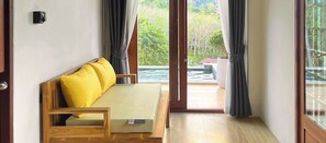 Una habitación con sofá de madera, una mesita y un ventanal corredero que da a un espacio exterior con piscina.
