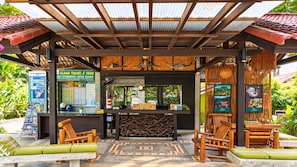 A covered outdoor seating area with wooden furniture and a counter displaying tourist information. - Alama Sea Village Resort (Ko Lanta)