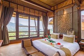 A spacious bedroom with a large bed, wooden beams, a view of the mountains, and a woven wall decoration.