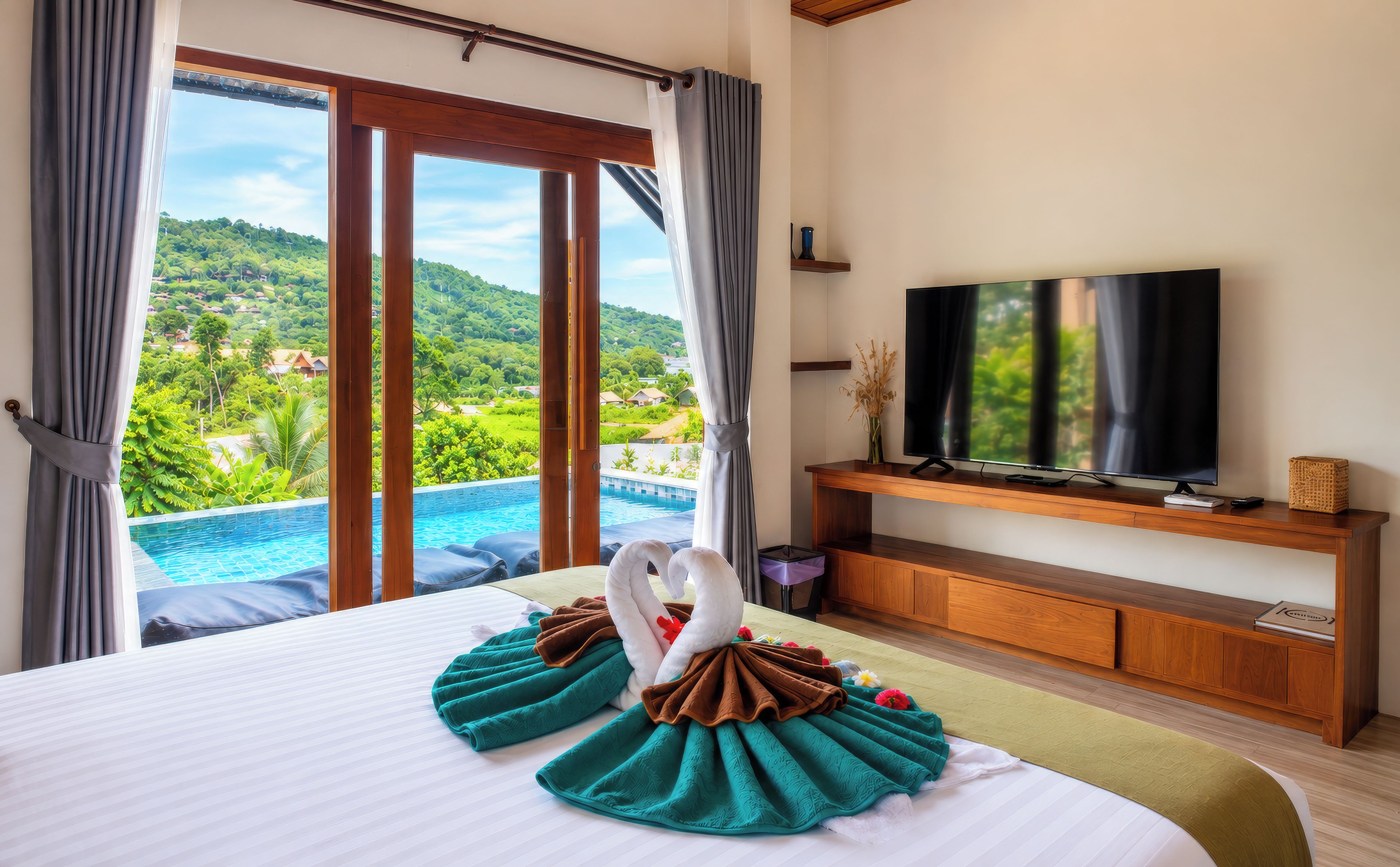 A hotel room with a large bed, a television on a wooden stand, and a view of a swimming pool and greenery.