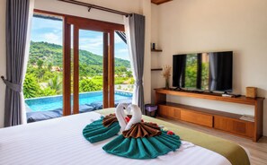 A hotel room with a large bed, a television on a wooden stand, and a view of a swimming pool and greenery. - Alama Sea Village Resort (Ko Lanta)