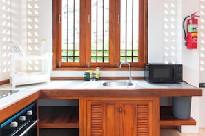 A compact kitchen with a built-in sink, a microwave, and a stove. - Alama Sea Village Resort (Ko Lanta)