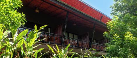 A building with a red roof, a balcony with a railing, and surrounding greenery.