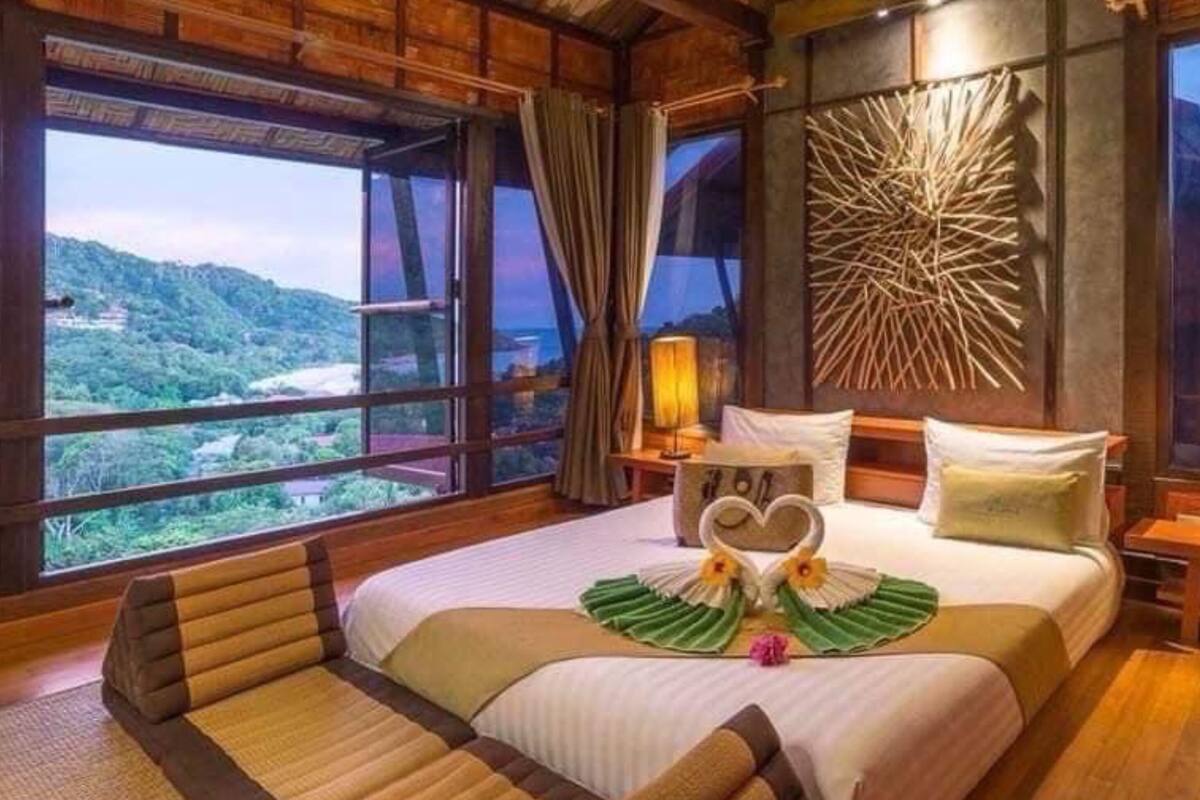 A bedroom with a large bed, wooden headboard, and a view of a mountainous landscape. There are two bedside tables with lamps.
