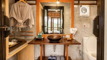 A bathroom with a wooden vanity, a large mirror, a sink, a toilet, and a hanging robe.