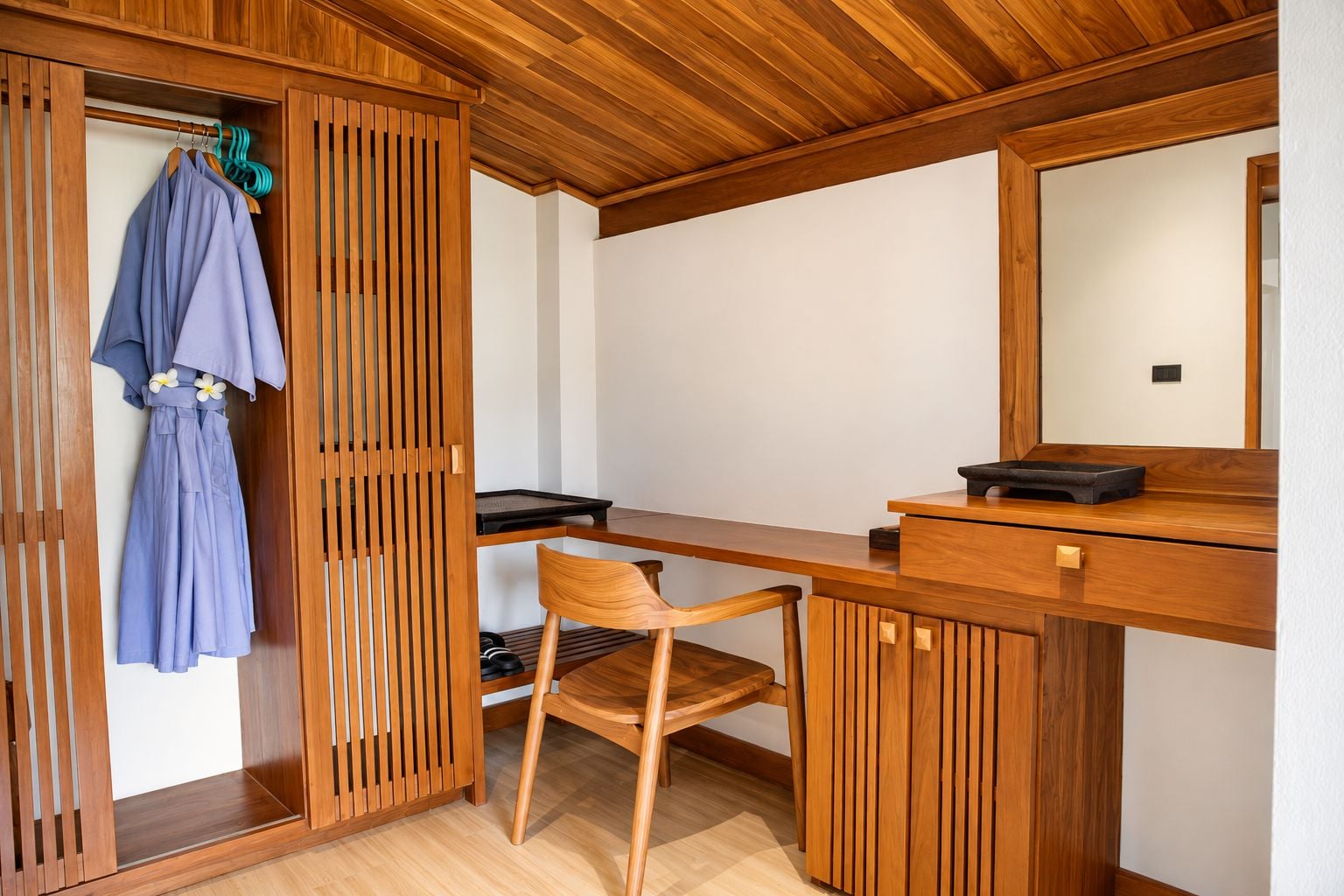 Una habitación de madera con escritorio, silla y un perchero con una bata.