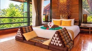A hotel room with a large bed, a wooden headboard, and a view of greenery outside.