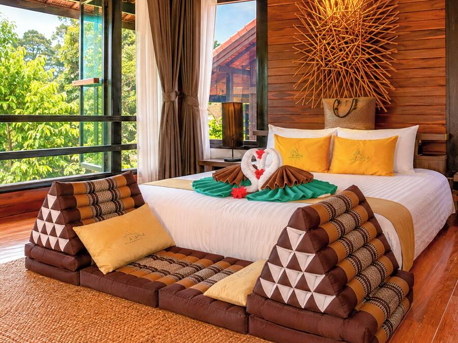 A hotel room with a large bed, a wooden headboard, and a view of greenery outside.