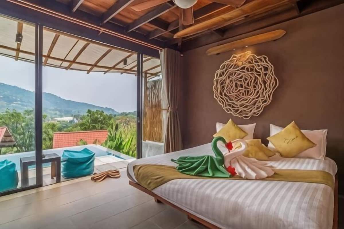 A bedroom with a bed, pillows, a decorative wall piece, and a view of greenery.