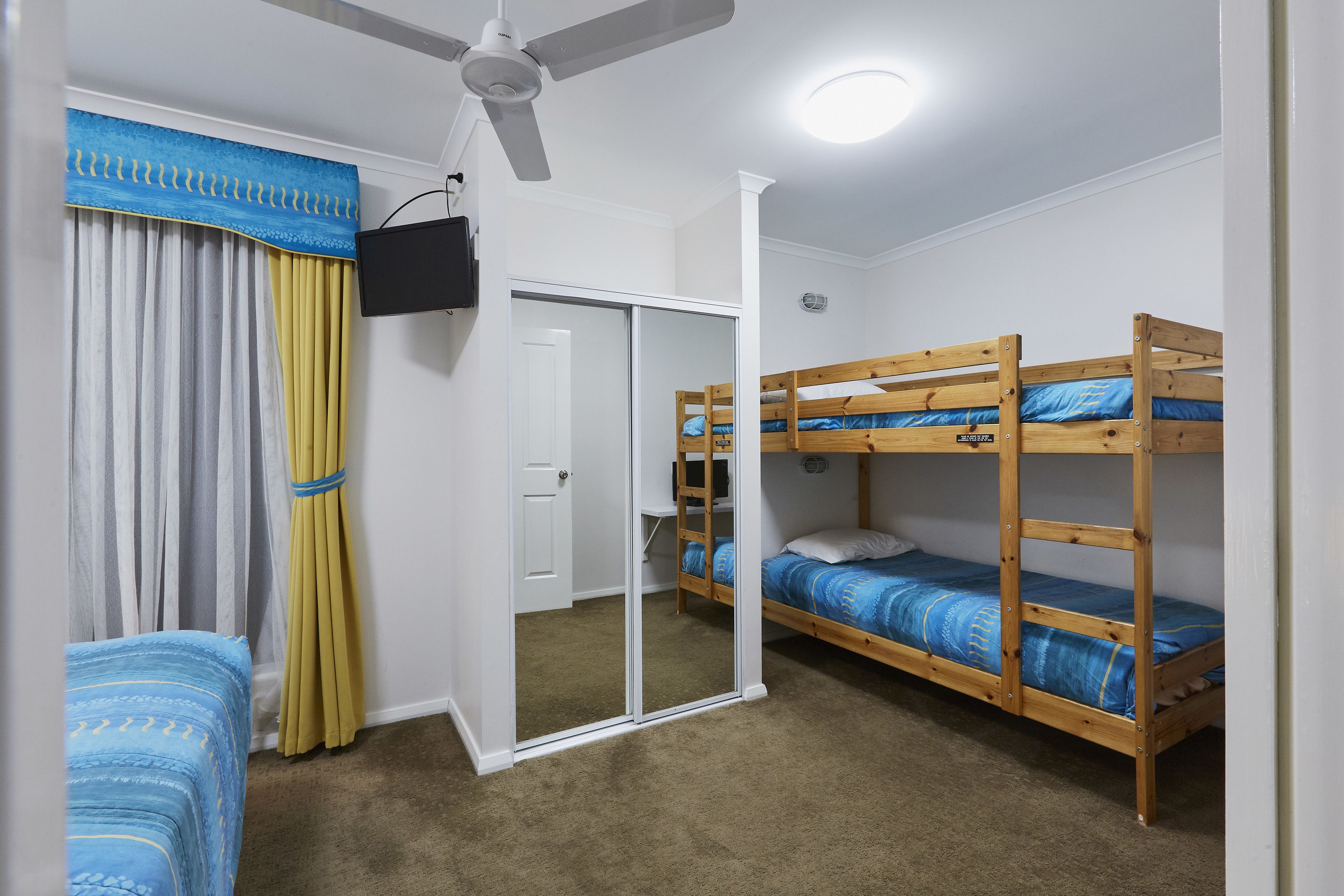 A room with bunk beds, a ceiling fan, a TV, and a sliding door.