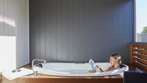 A person relaxing in a hot tub with a book, wooden floor, and a window with blinds. - Discovery Parks - West Busselton (West Busselton)