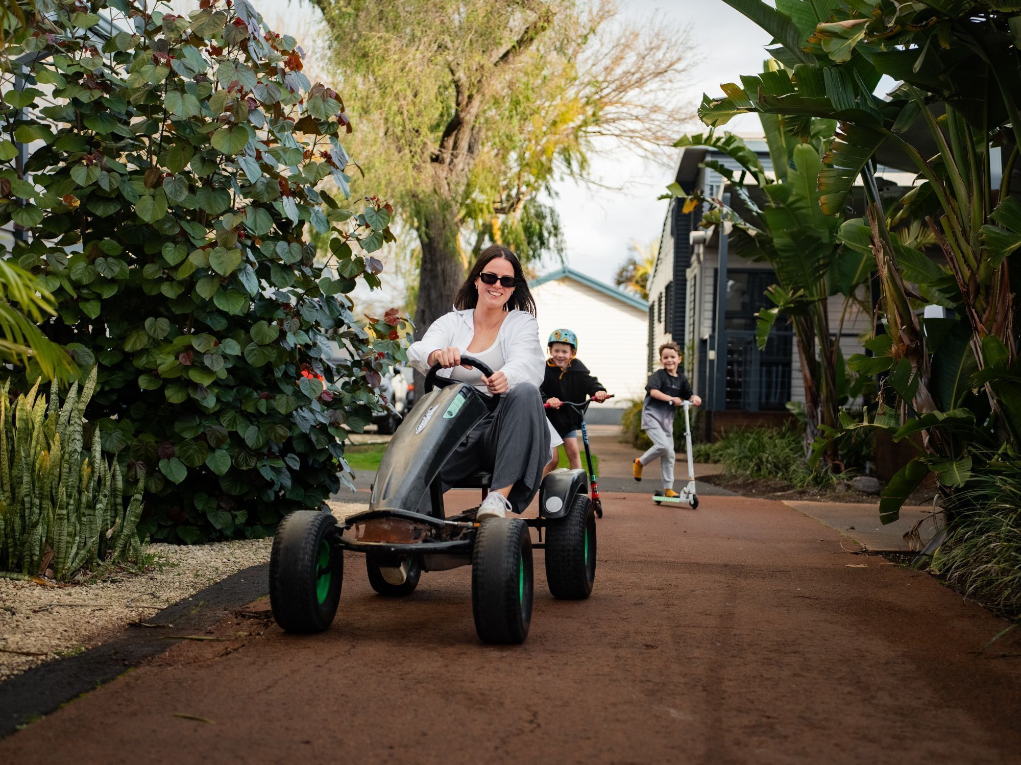 A person riding a three-wheeled electric vehicle on a paved path surrounded by lush greenery and banana plants.
