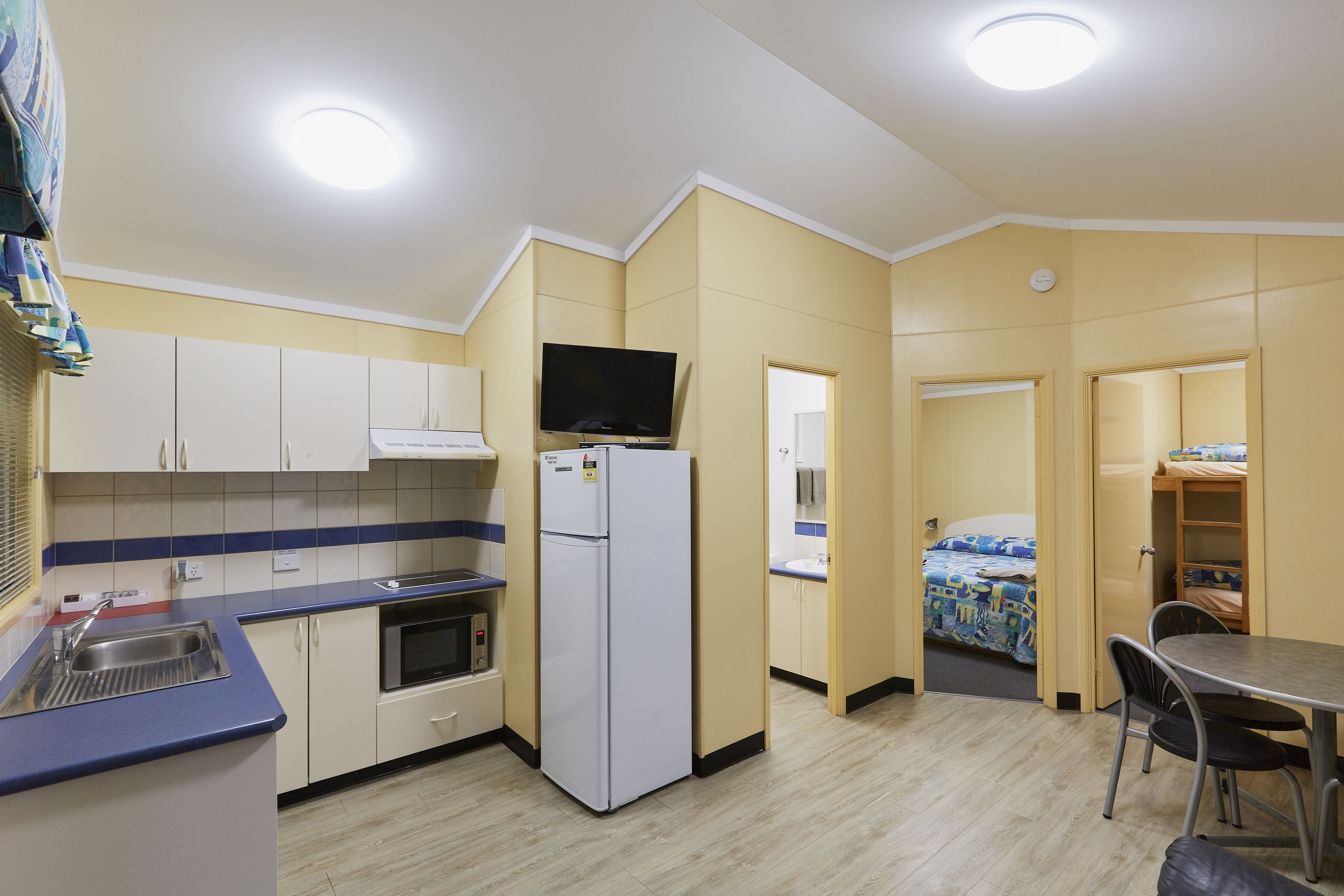 A compact kitchen with a refrigerator, microwave, and sink. There is a dining area with a table and chairs.