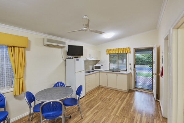 A compact kitchen with a microwave, a ceiling fan, and a dining area with blue chairs and a table. - Discovery Parks - West Busselton (West Busselton)
