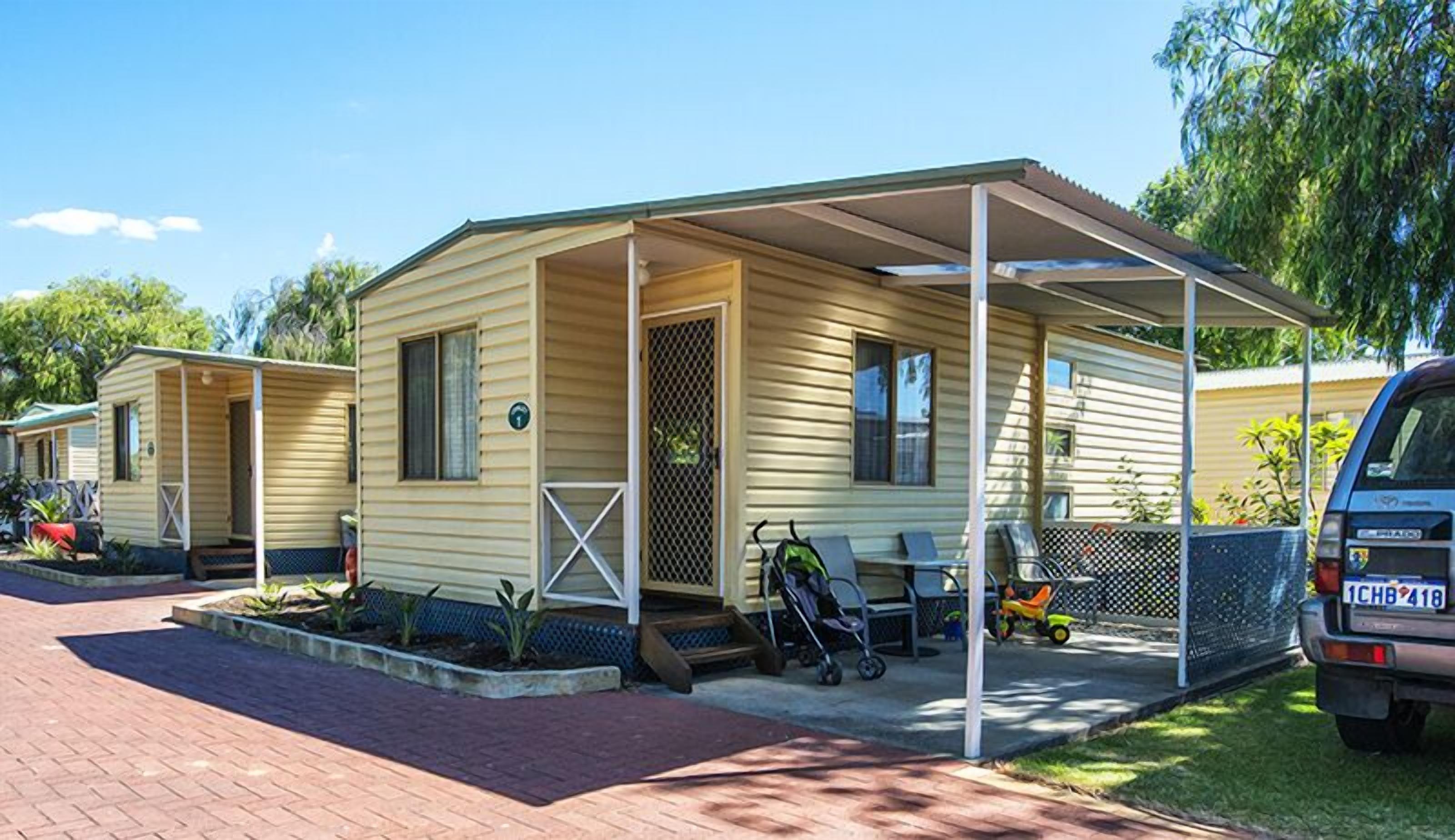 A mobile home with a covered porch, a small garden, and a parked car.