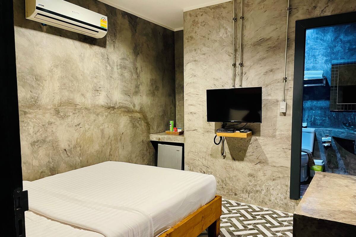 A modern hotel room with a bed, a small desk, a TV, and an air conditioning unit.