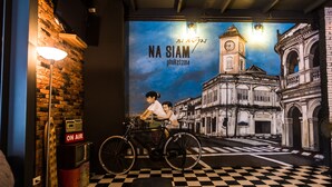 A room with a checkered floor, a wall-mounted TV, and a poster of a cityscape with a bicycle. - Na Siam Guesthouse (Phuket)