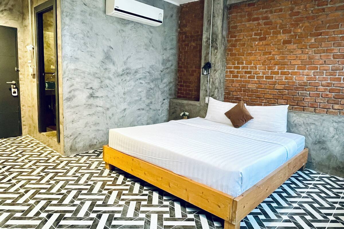 A bedroom with a bed, a brick wall, and a patterned floor.