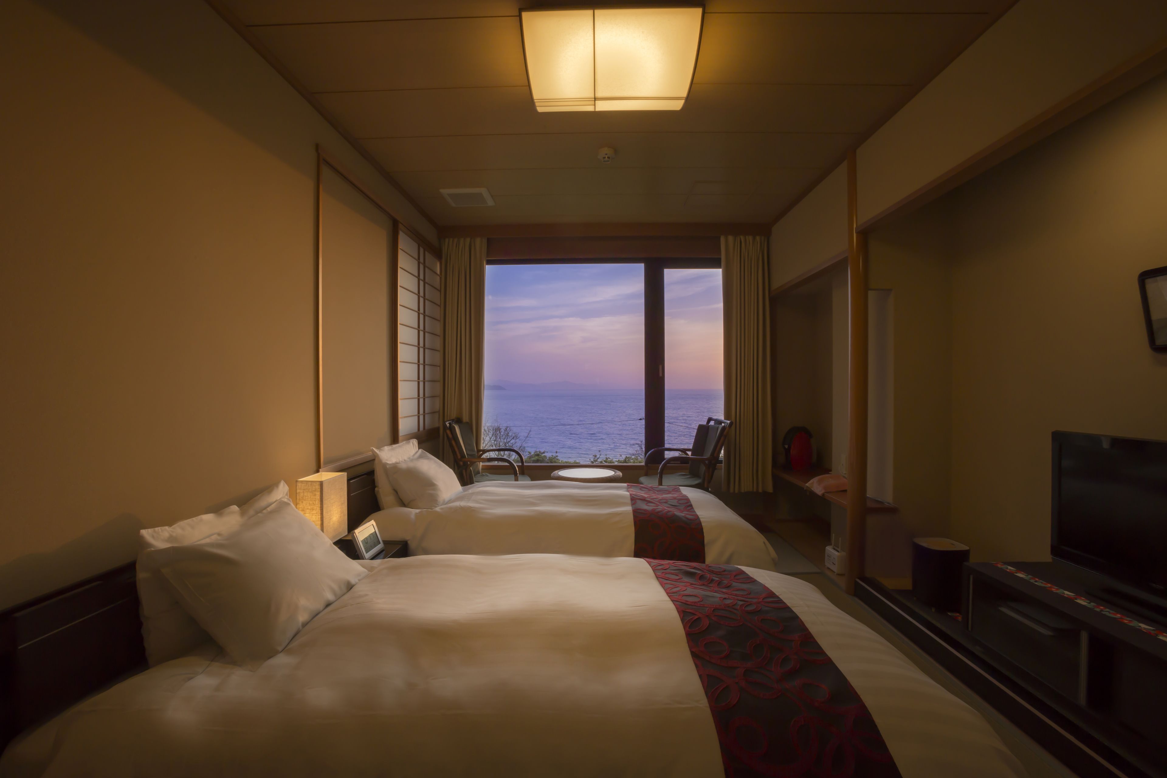 Habitación de hotel con dos camas, un televisor, una mesita y vista al océano.