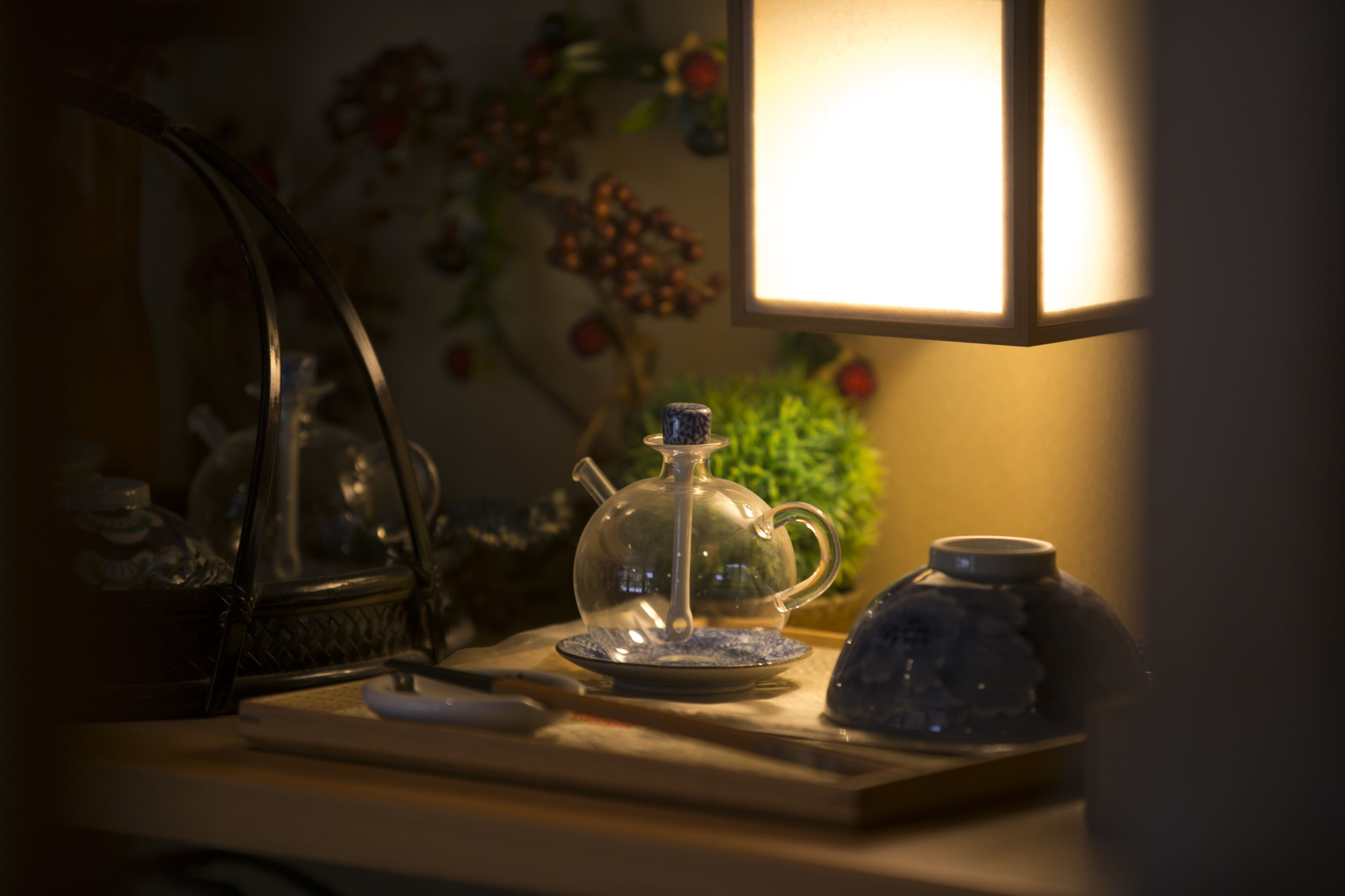 Une table avec une théière, une tasse et une soucoupe, éclairée par une lampe.