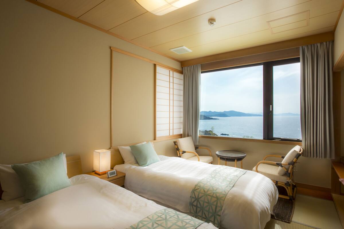 Ett hotellrum med två sängar, ett litet bord, en stol och utsikt över havet.