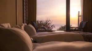 Ein Hotelzimmer mit zwei Betten, Meerblick und einem Sessel am Fenster.
