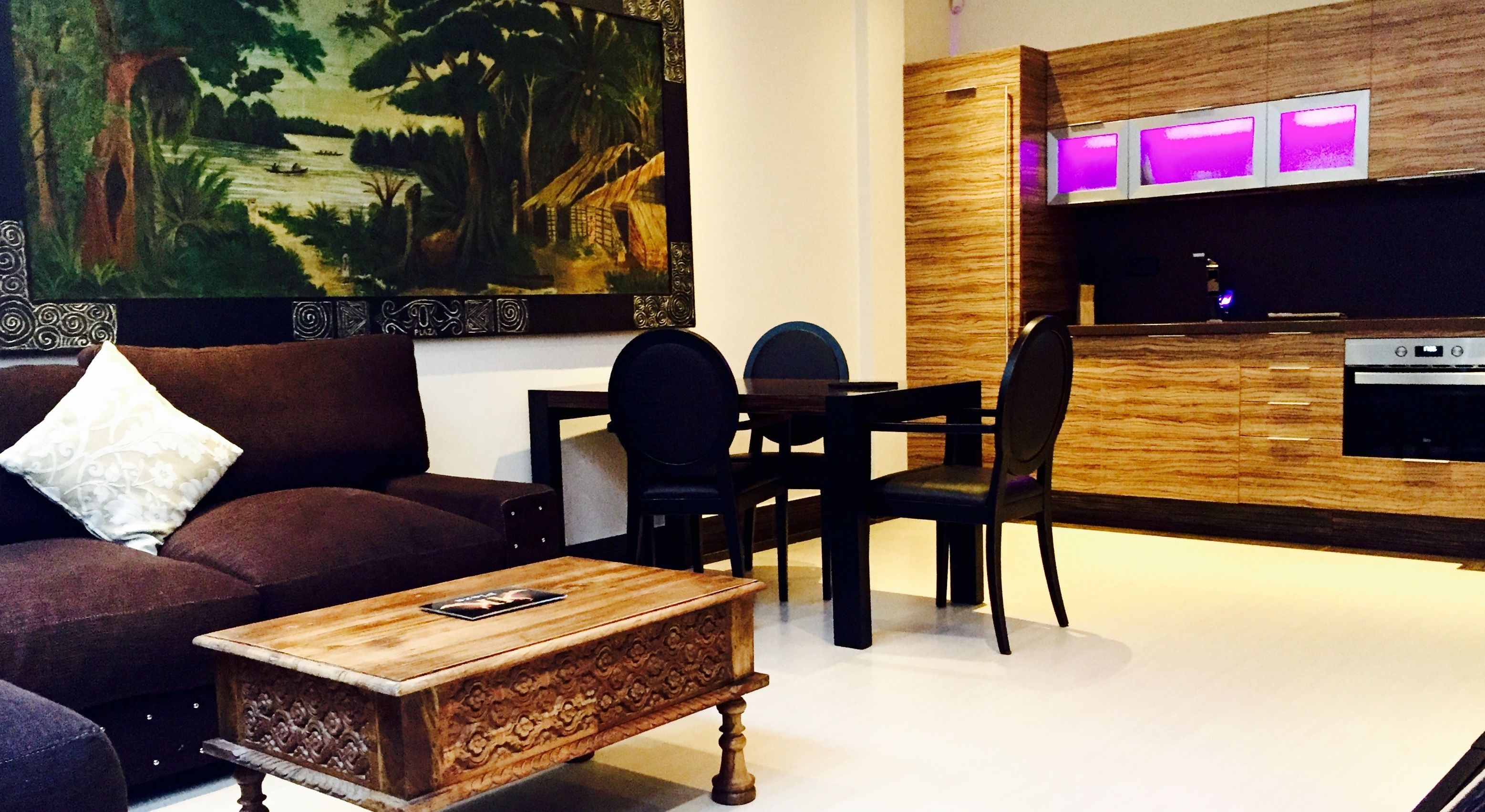 Un soggiorno moderno con divano, tavolino e zona pranzo con sedie e tavolo. Un quadro appeso al muro e un angolo cottura con un mobiletto in legno e un televisore.