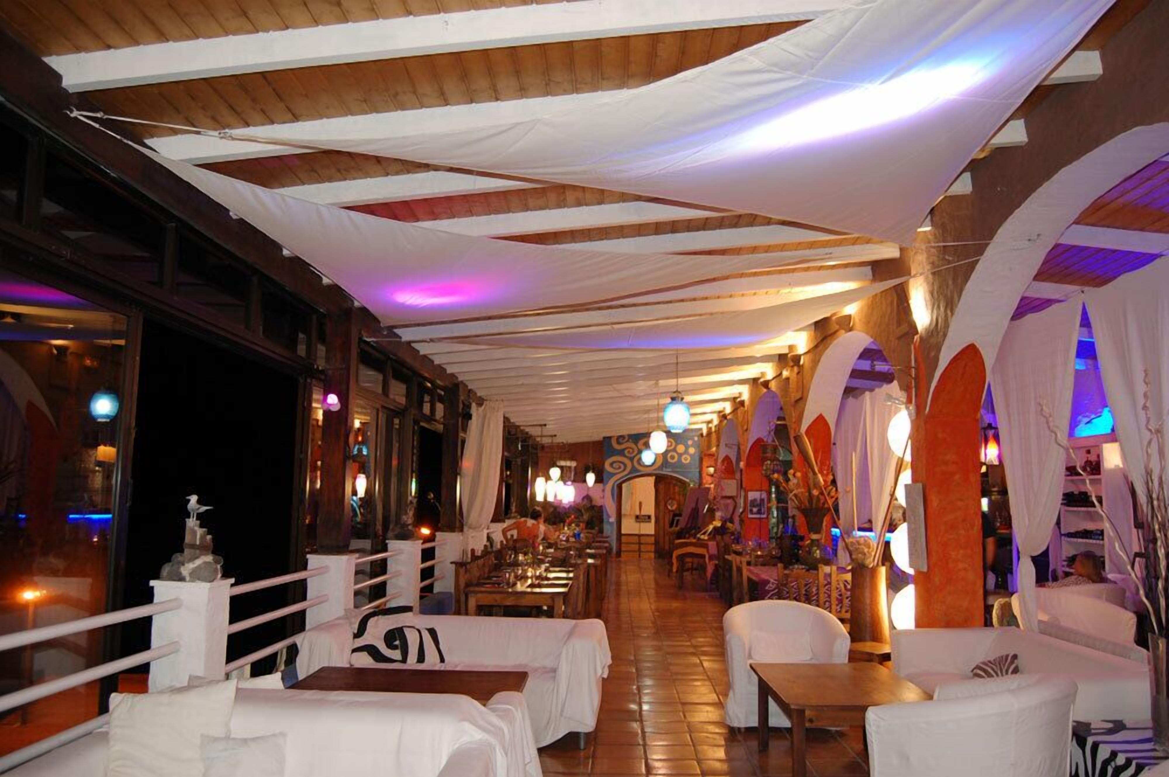 A restaurant with white tablecloths, wooden beams, and hanging lights.