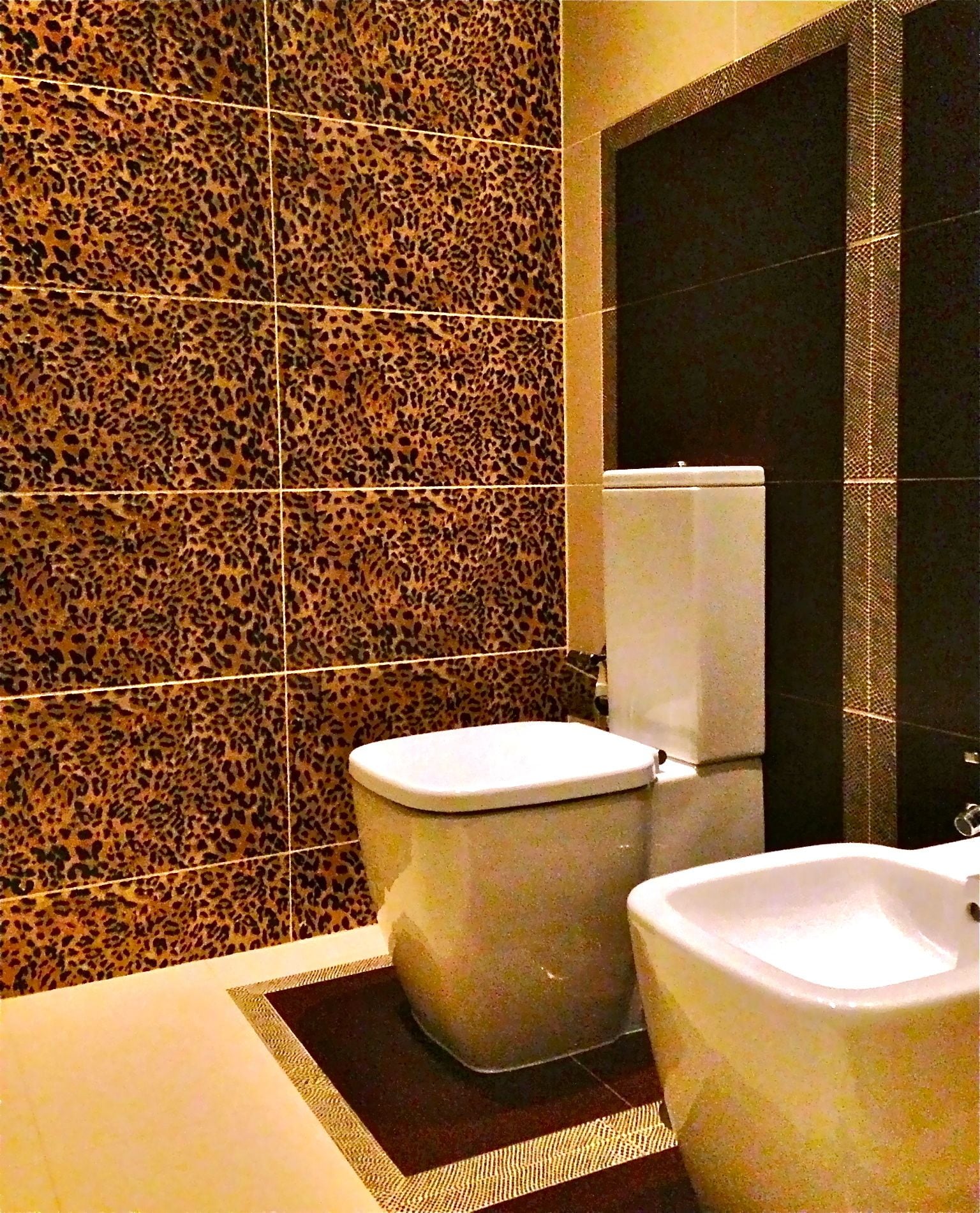 Un baño con pared de baldosas de estampado de leopardo, un inodoro y un lavabo.
