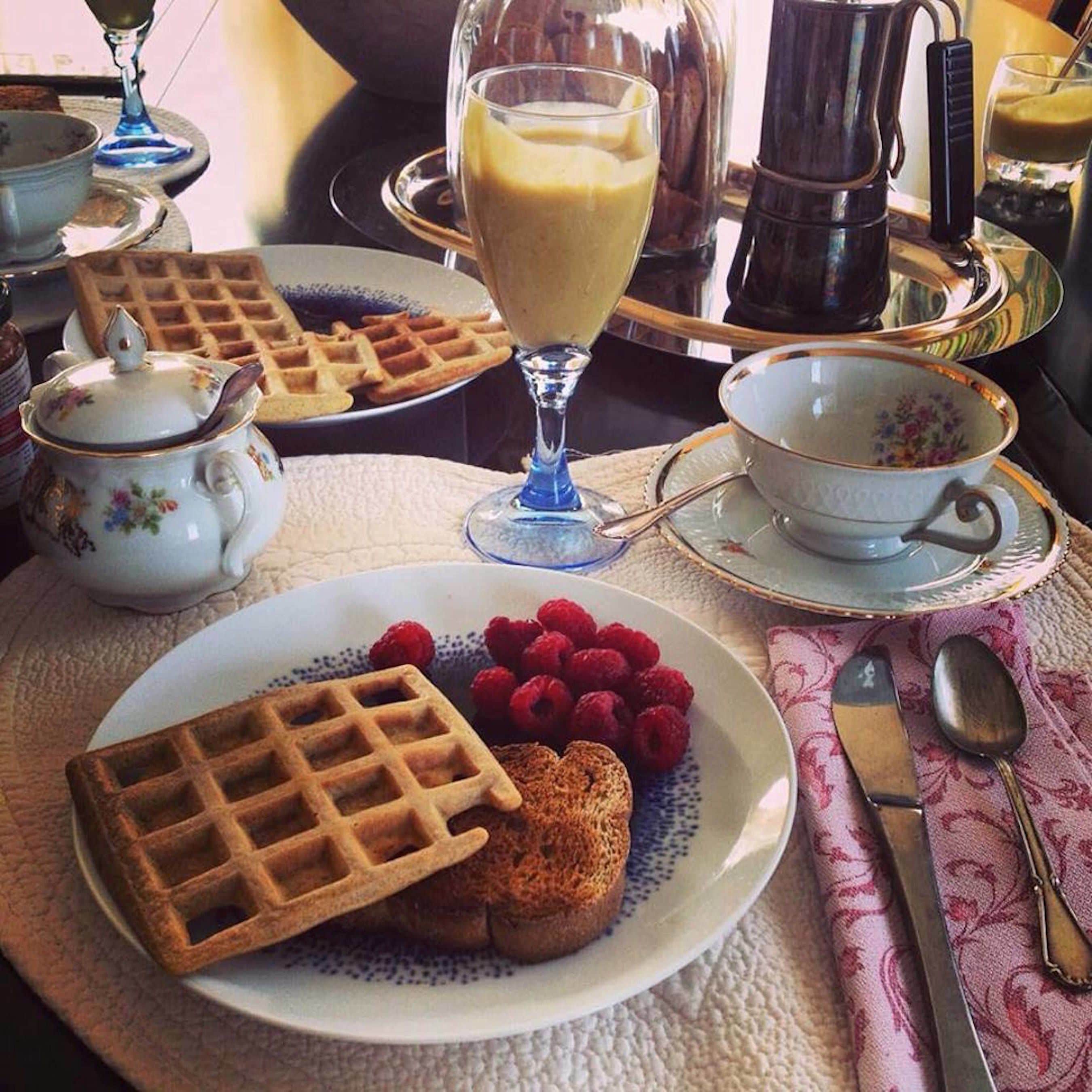 A breakfast setting with waffles, raspberries, and a glass of milk.