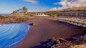 A beach with a rocky shoreline, a sandy area with lounge chairs, and a clear sky. - Rok Plaza - Only Adults (Guia de Isora)