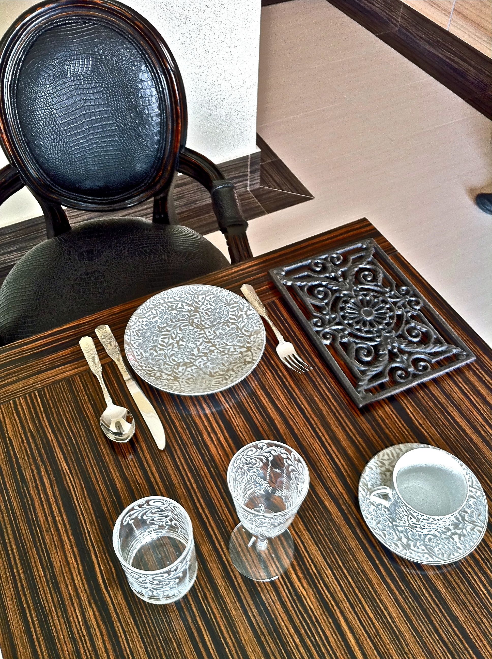 Une table à manger dressée avec des assiettes, des couverts et des verres, une chaise et un plateau décoratif en arrière-plan.