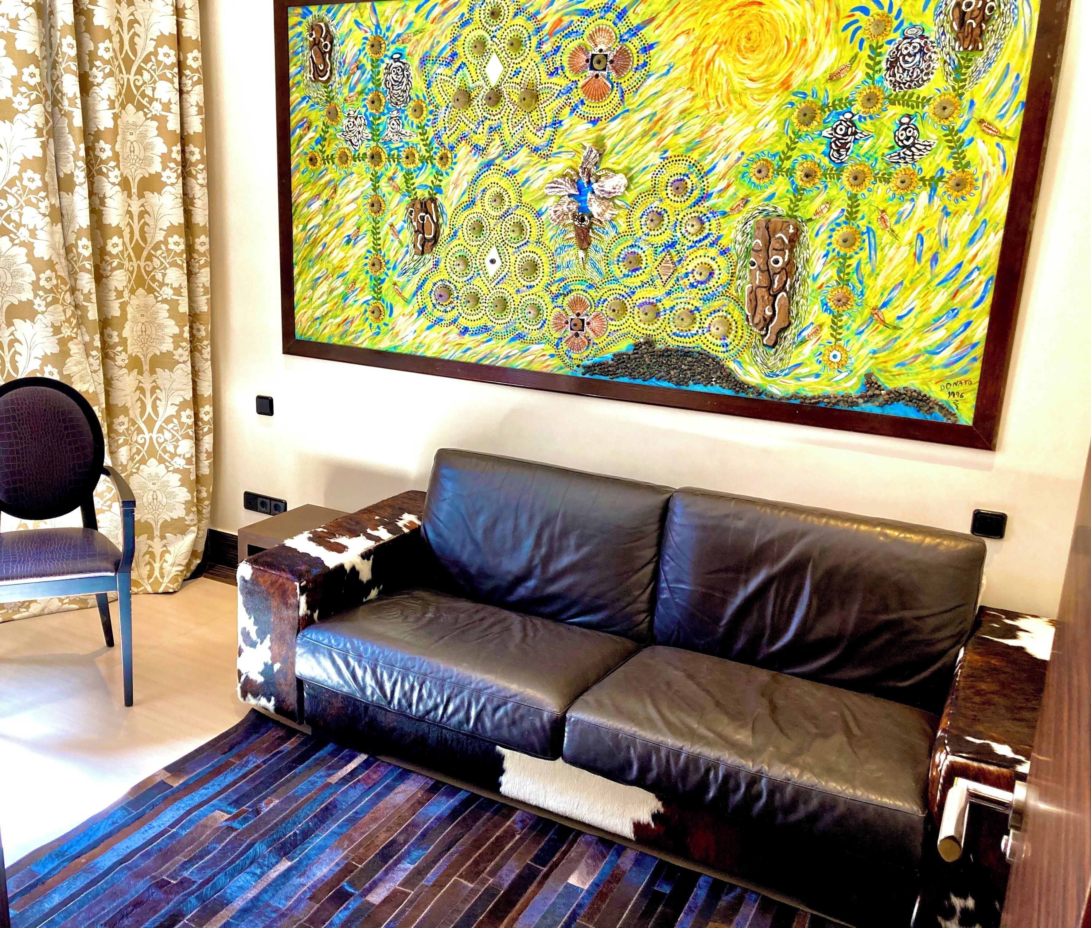 A living room with a black leather sofa, a patterned armchair, a colorful abstract painting, and a striped rug.