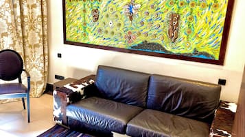 Una sala de estar con un sofá de cuero negro, un sillón estampado, un cuadro abstracto de colores y un tapete a rayas.
