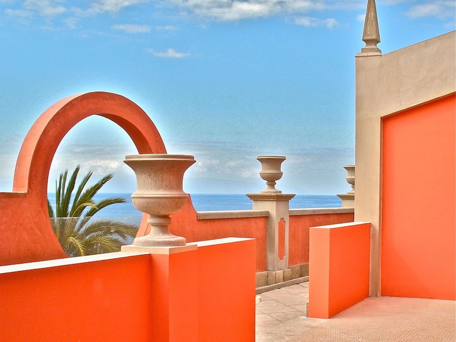 Una terraza con vista al mar, que presenta un arco rojo y balaustradas de estilo clásico.
