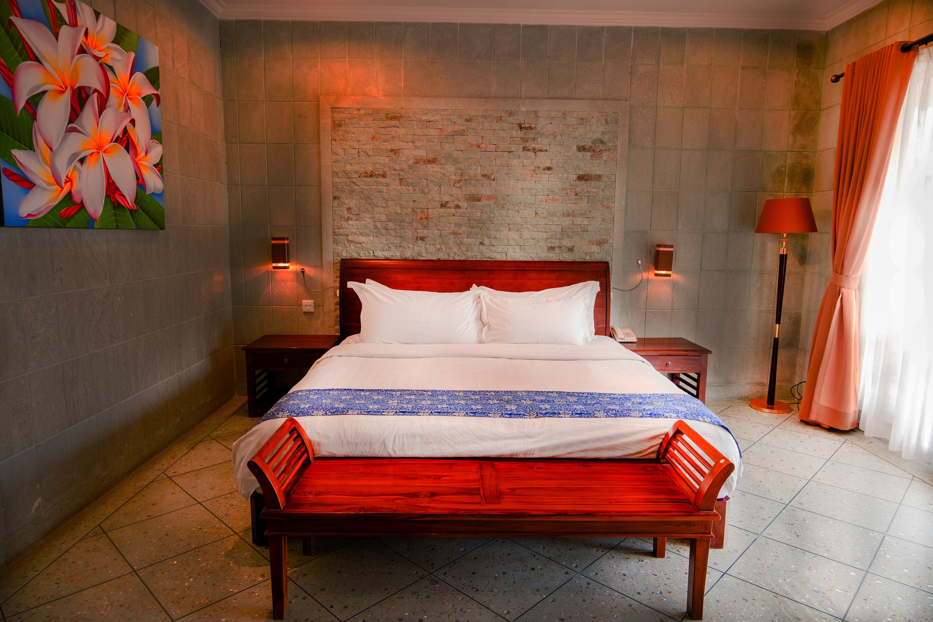 A neatly made bed with a wooden headboard, two bedside tables with lamps, and a large floral painting on the wall.