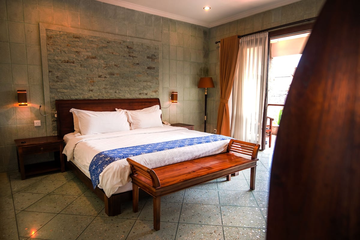 A hotel room with a large bed, wooden bench, two bedside tables, and a brick wall.