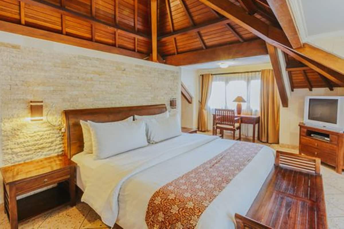 A room with a wooden ceiling, a bed with white bedding, a TV, and a small table.