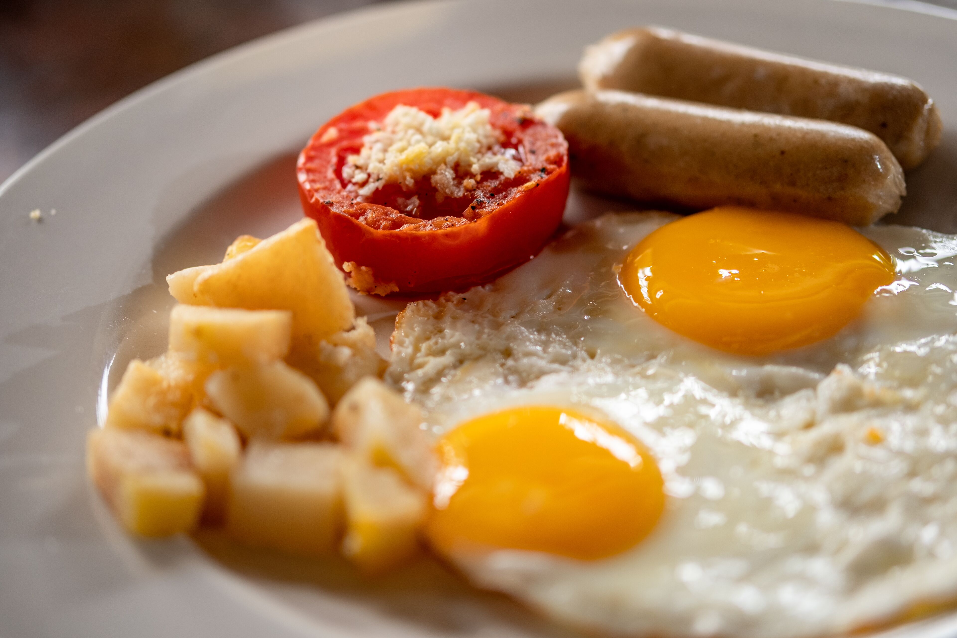 A plate with scrambled eggs, two fried eggs, a grilled tomato, cheese cubes, and two sausages.
