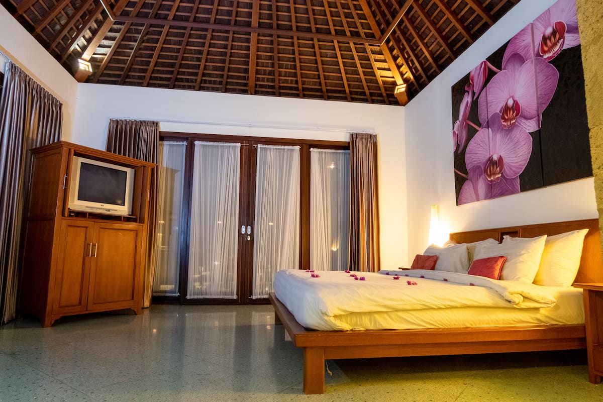 A bedroom with a wooden bed, a television on a cabinet, and a large orchid painting on the wall.