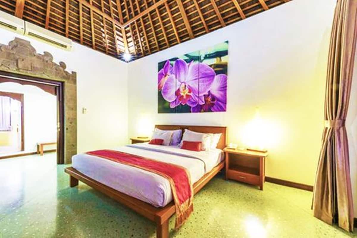 A hotel room with a wooden bed, a nightstand, a wall-mounted lamp, and a large floral artwork.
