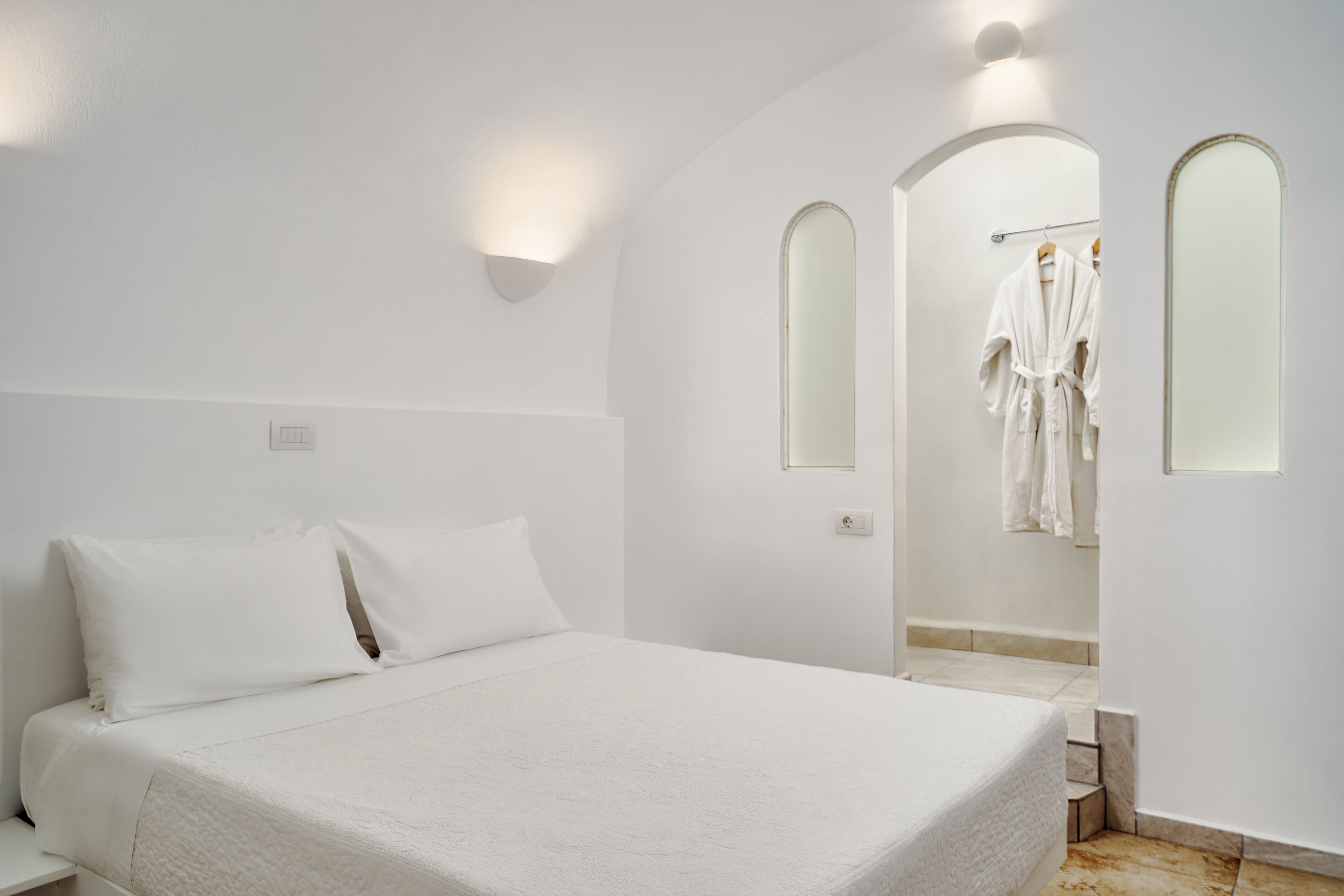 Une chambre à coucher avec un grand lit, une table de chevet et un dressing équipé d’un miroir et d’un porte-manteau.
