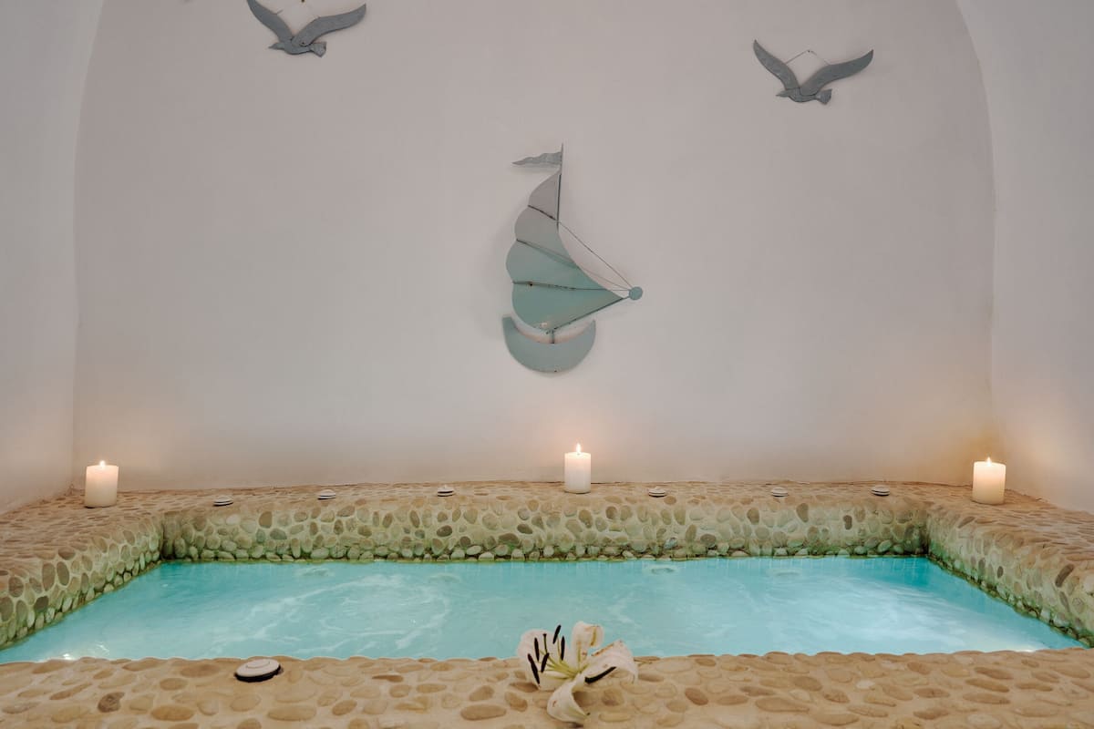 Un espace de bien-être doté d’une piscine bordée de pierres, de bougies et de sculptures d’oiseaux fixées aux murs.